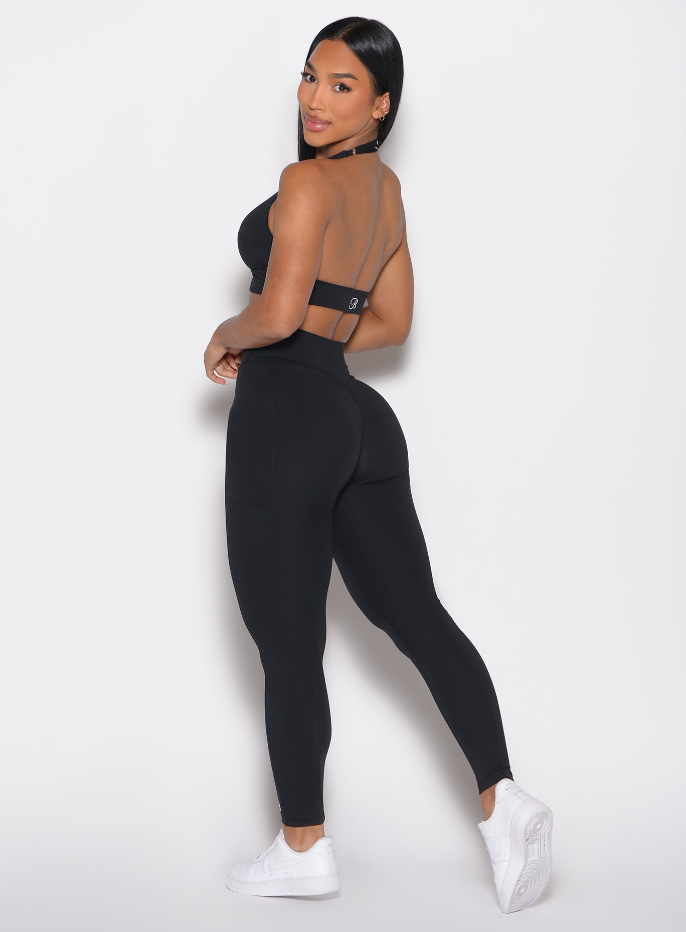 left side profile view of a model looking over her shoulder wearing the Sculpt Knot Leggings in black color
