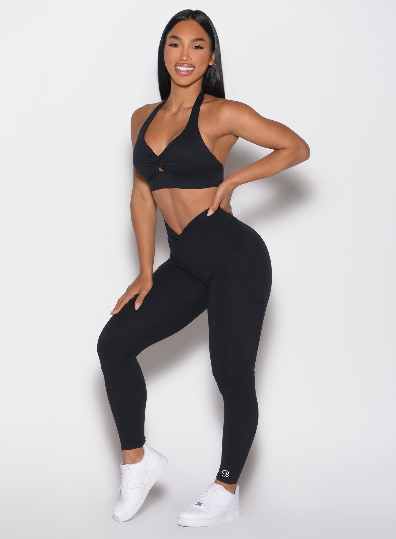 front profile view of a model with one hand on her waist wearing the Sculpt Knot Leggings in black color
