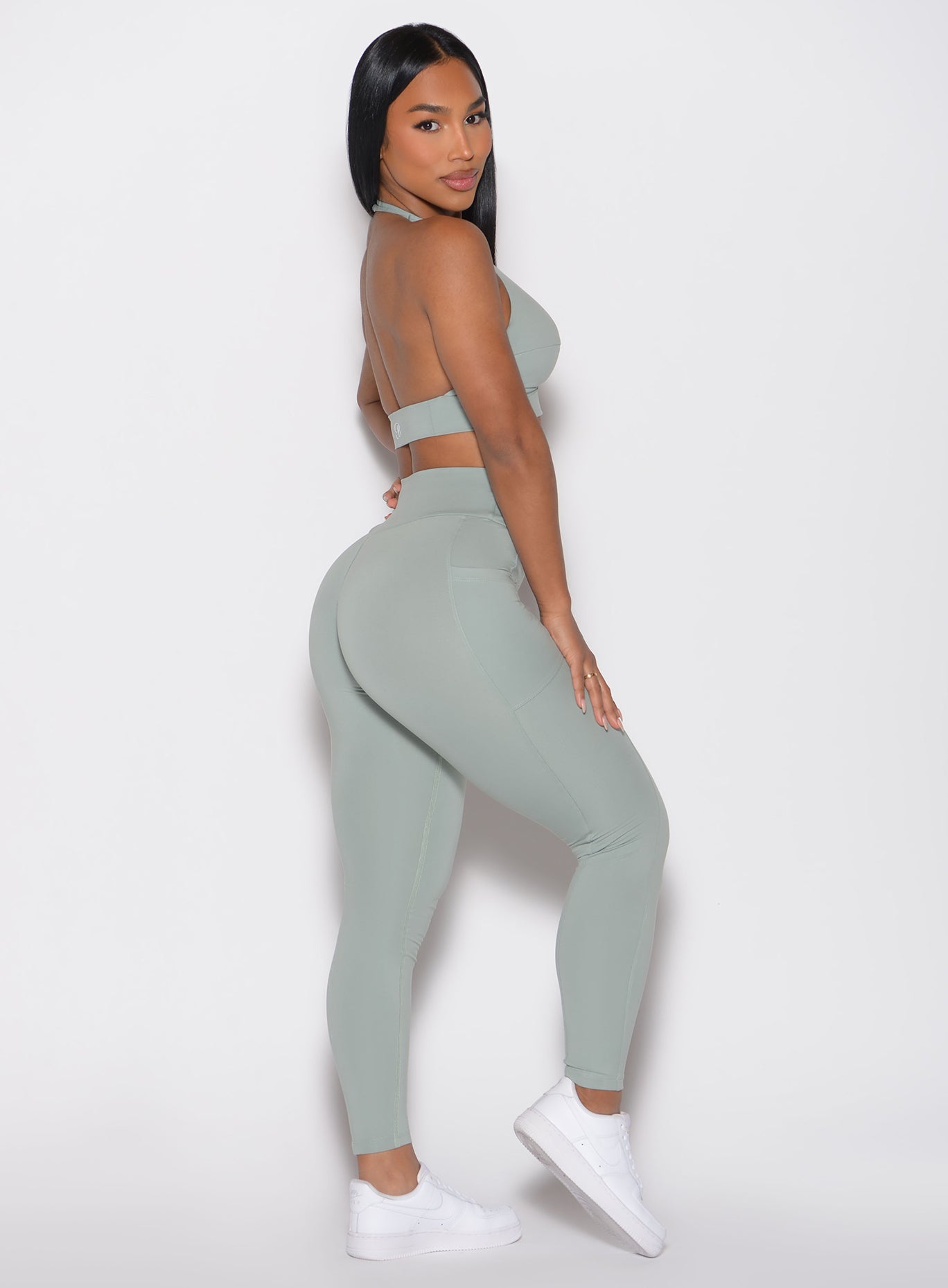 right side profile view of a model looking over her shoulder wearing the Sculpt Knot Leggings in Iceberg Green color