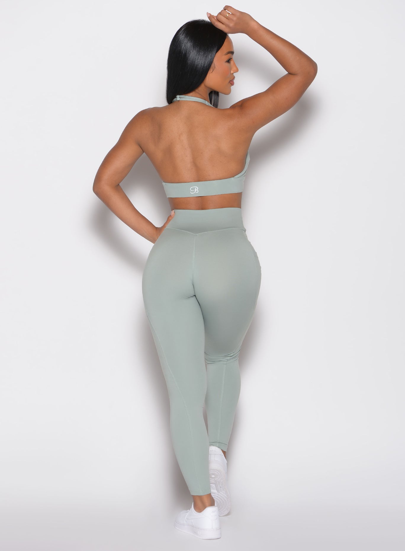 back profile view of a model facing to the right side wearing the Sculpt Knot Leggings in Iceberg Green color