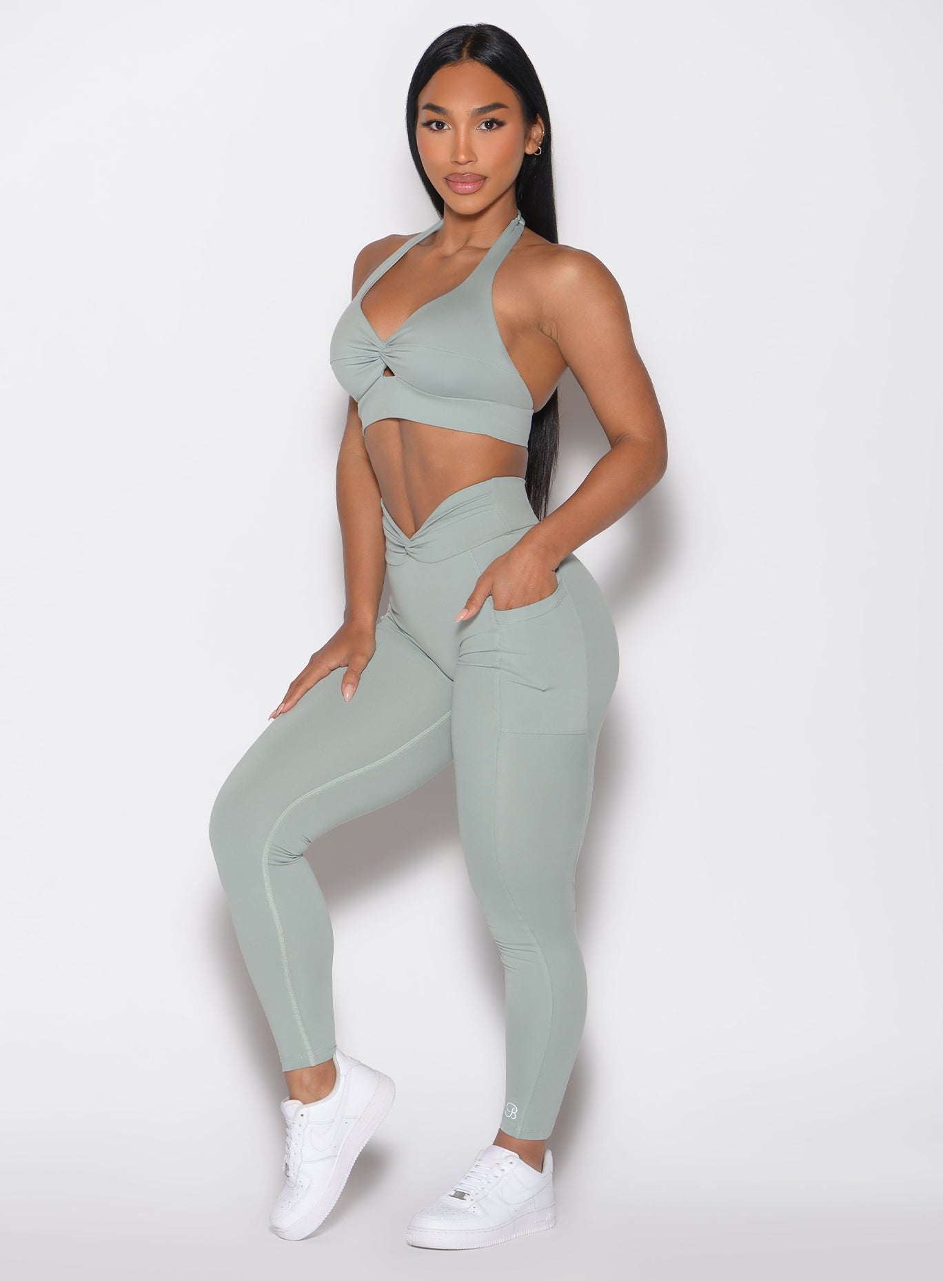 front left side profile view of a model with one hand inside the pocket wearing the Sculpt Knot Leggings in Iceberg Green color