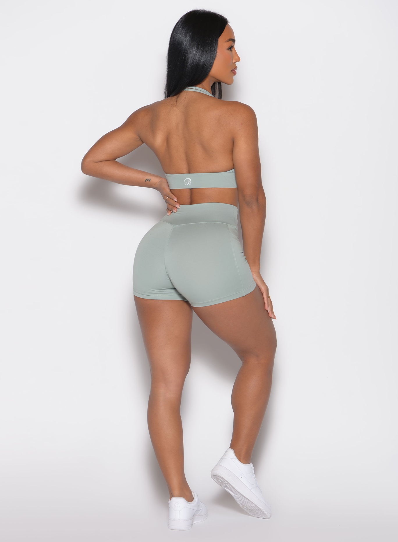 back profile view of a model facing to the right side with one hand on her waist wearing the Sculpt Knot Shorts in iceberg green color