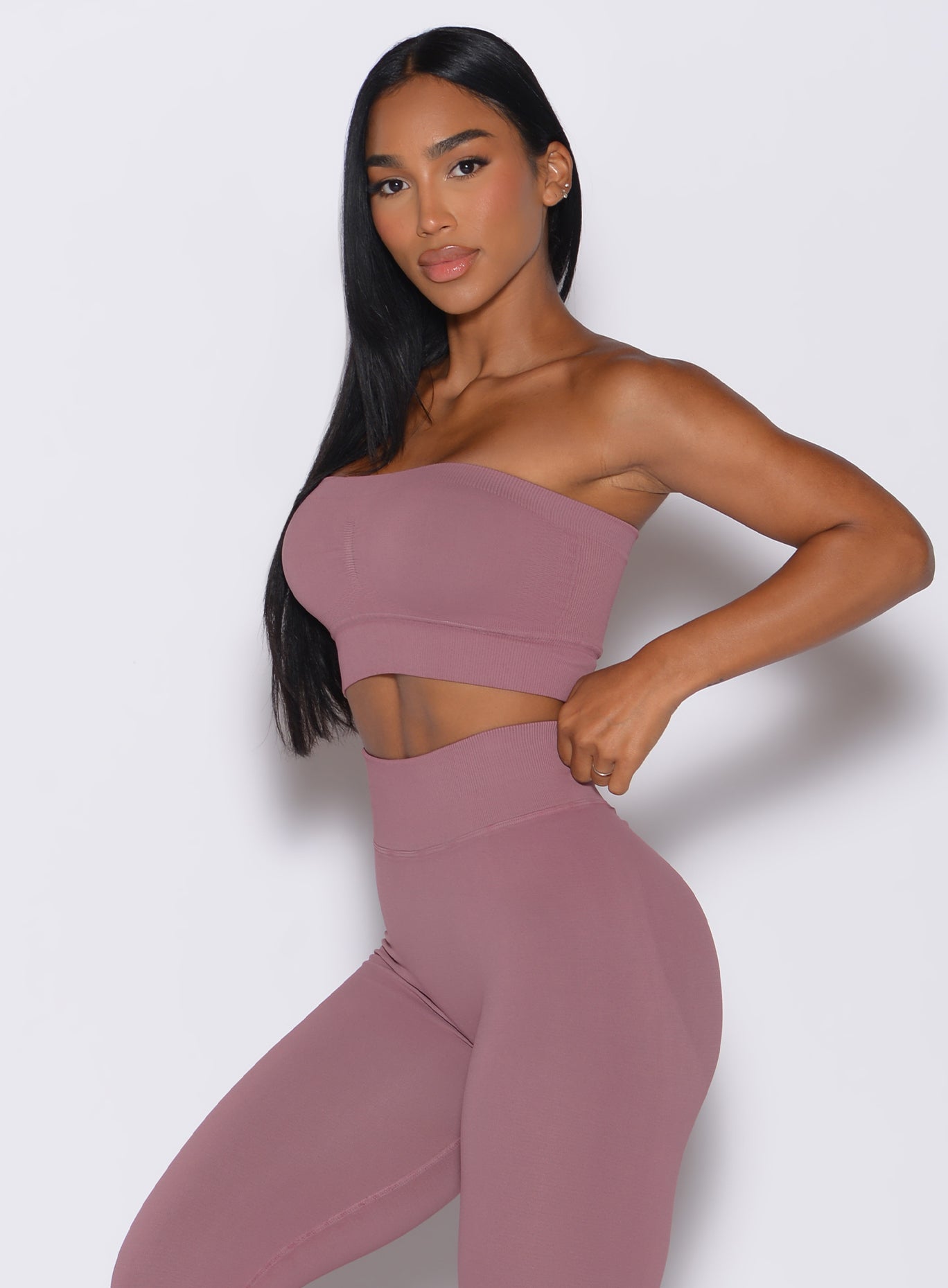 Left side profile view of a model facing to her left wearing our seamless bandeau in satin color along with the matching leggings