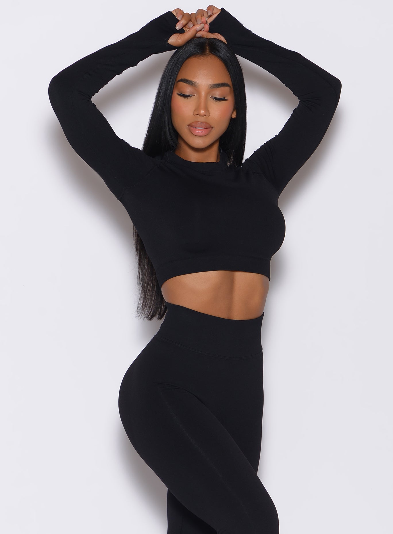 front profile view of a model with her hands over her head wearing our black seamless pullover along with a matching leggings