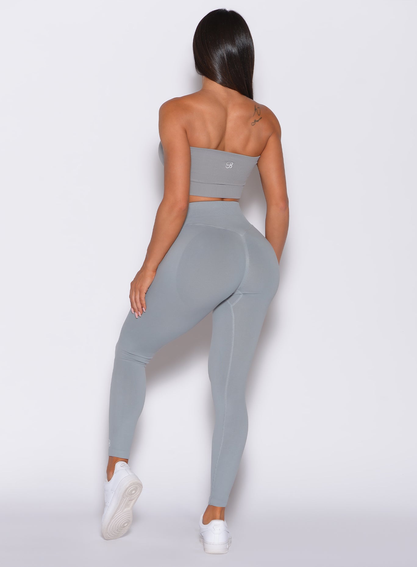 back profile view of a model wearing our cheeky seamless leggings in fog gray color along with a matching bandeau