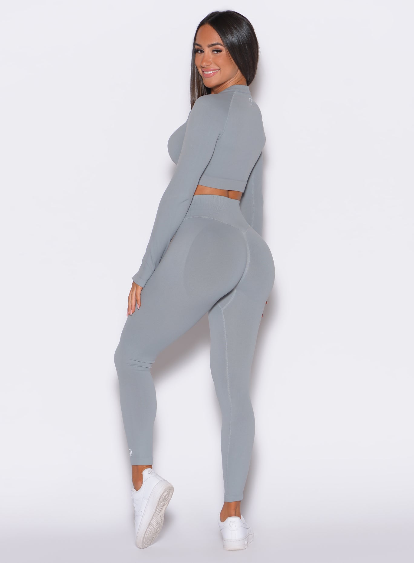 back profile view of a model angled left wearing our cheeky seamless leggings in fog gray color along with a matching pullover