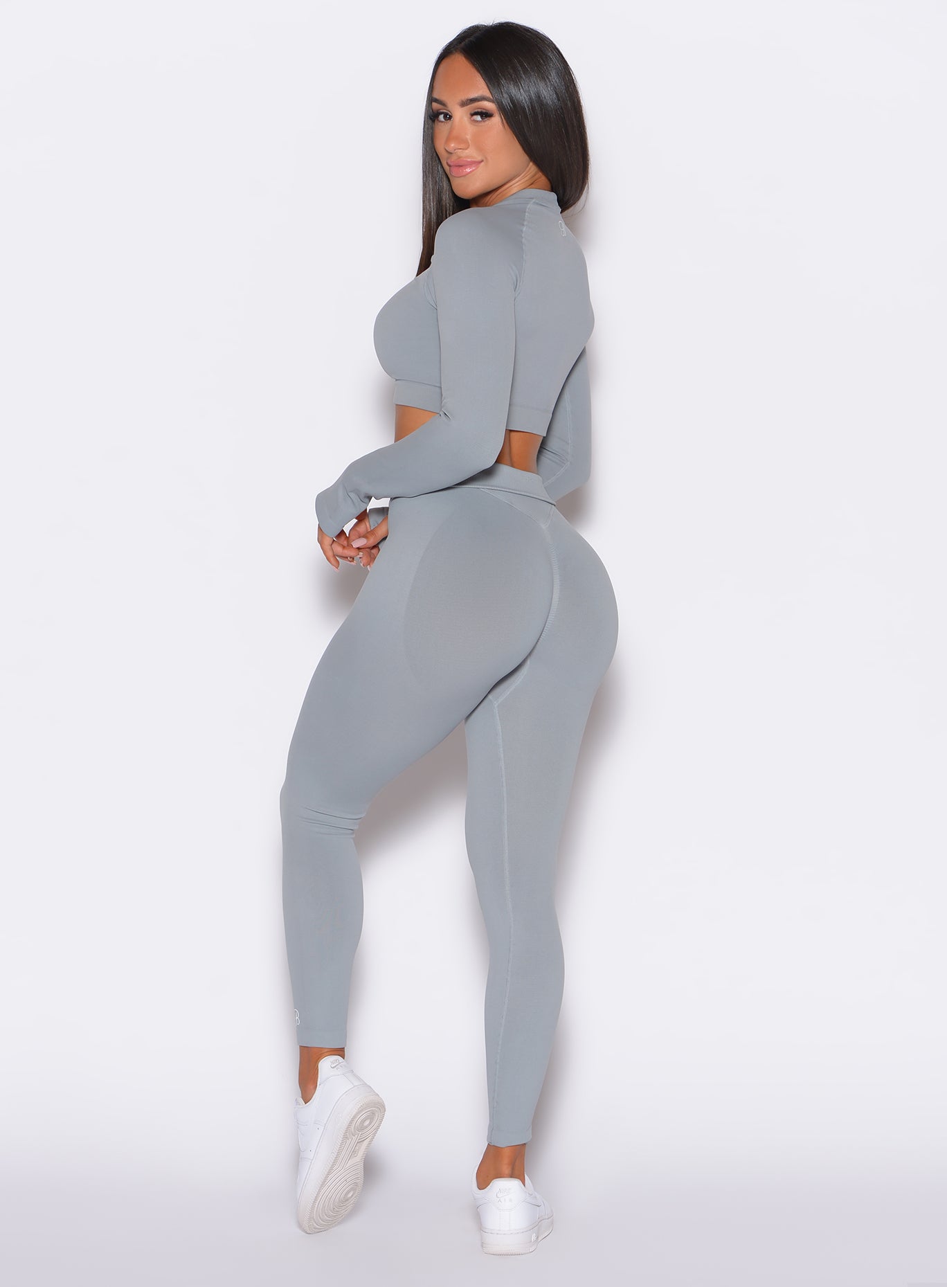 left side profile view of a model facing to her left wearing our cheeky seamless leggings in fog gray and a matching pullover