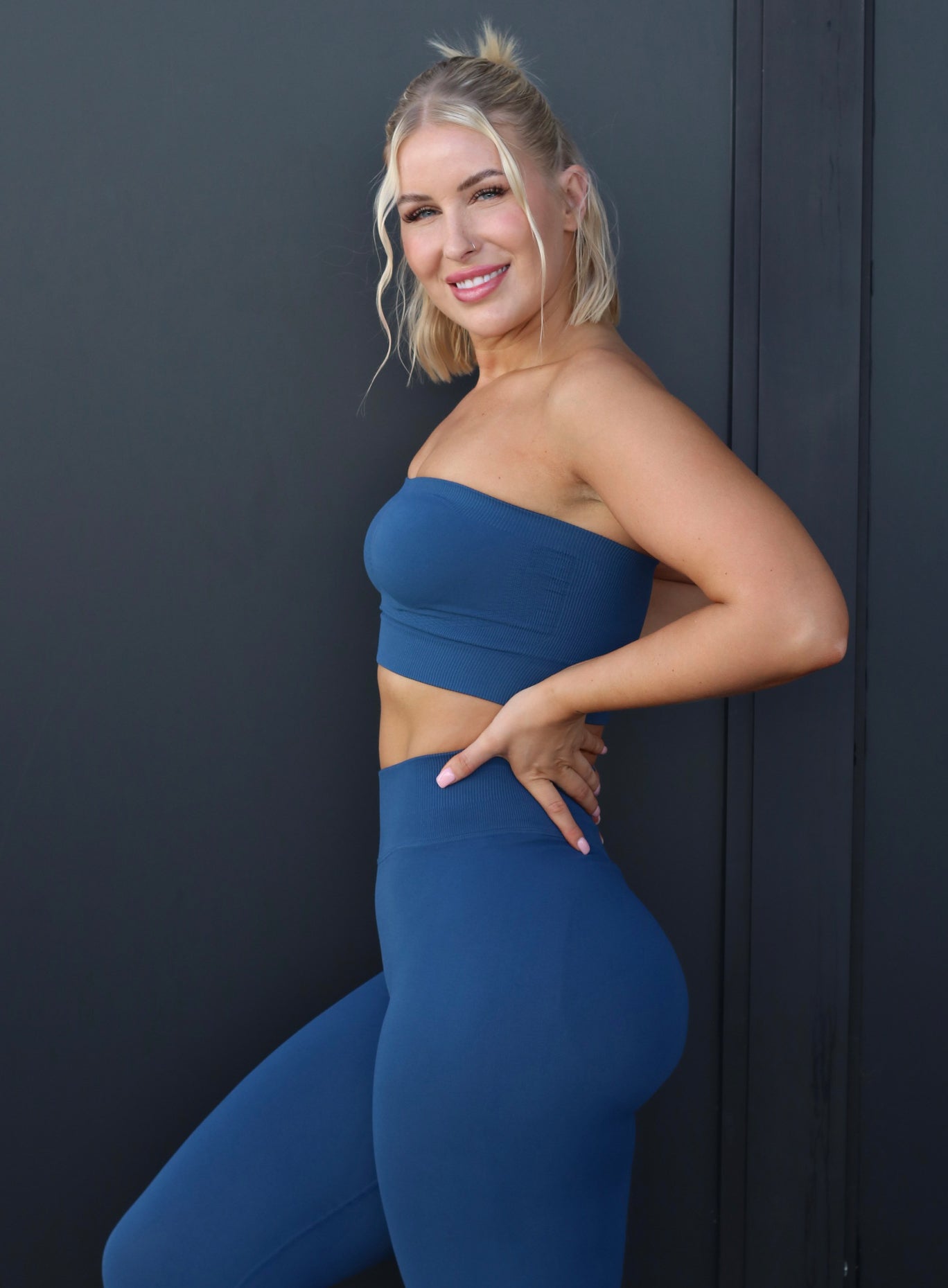 Left side profile view of a model with her hands on waist wearing our cheeky seamless leggings in galaxy color along with the matching bandeau