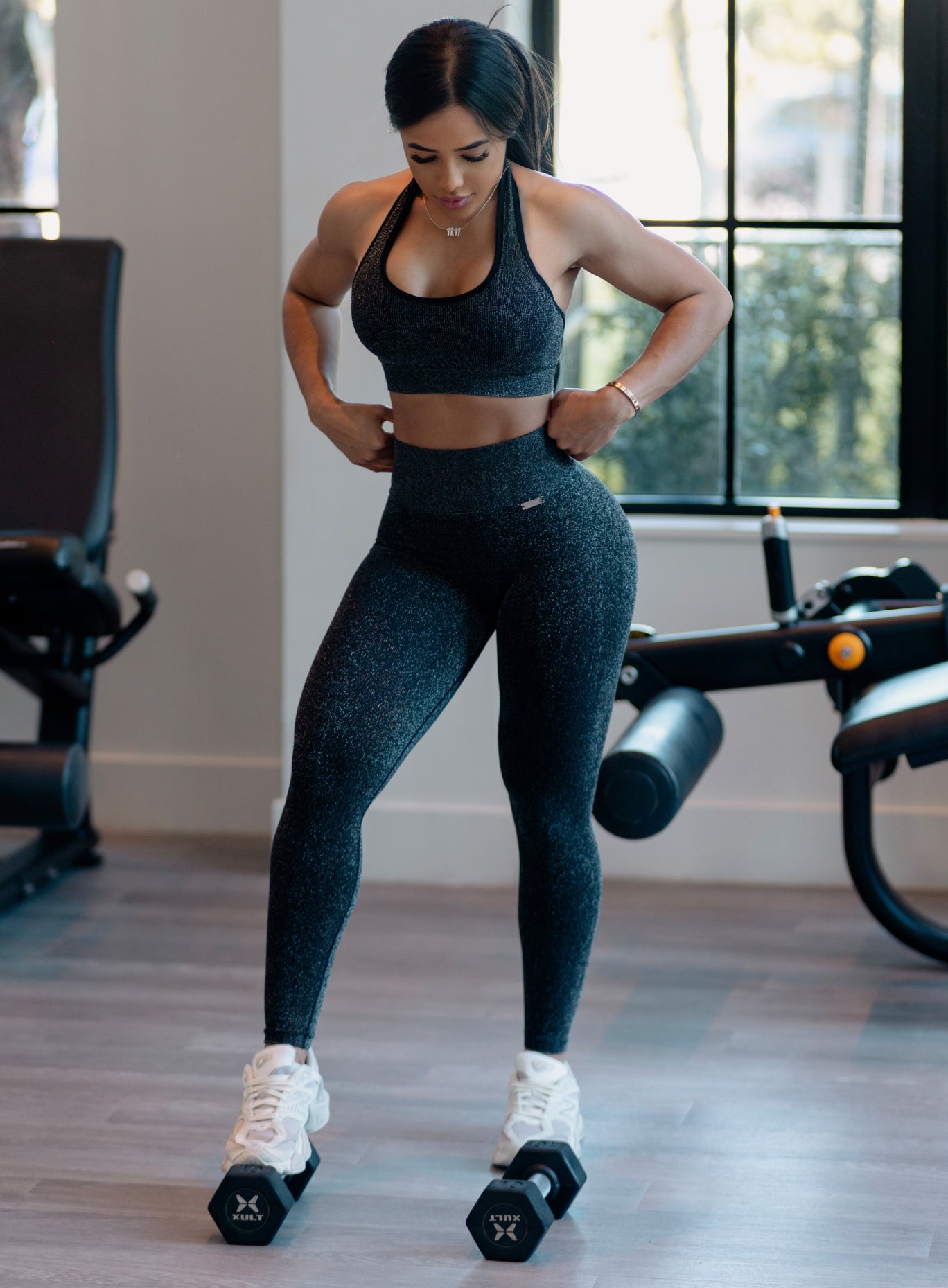 front profile view of a model at the gym facing down wearing the Shimmer V Back Leggings in Black star color