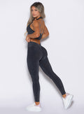 left side profile view of a model looking over her shoulder wearing the Shimmer V Back Leggings in Black star color