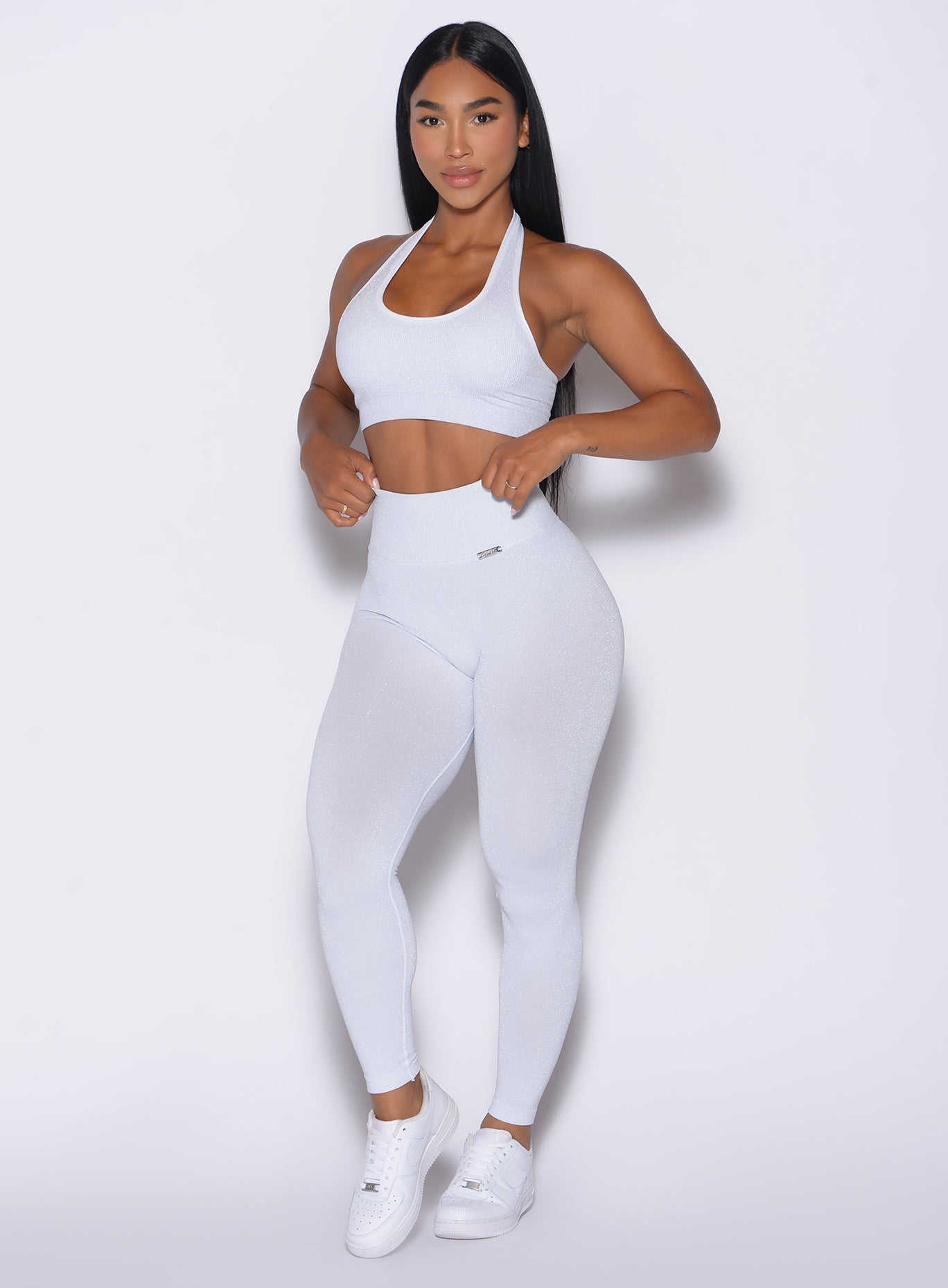 front left side profile view of a model adjusting the waistband of the leggings wearing the Shimmer V Back Leggings in White star color