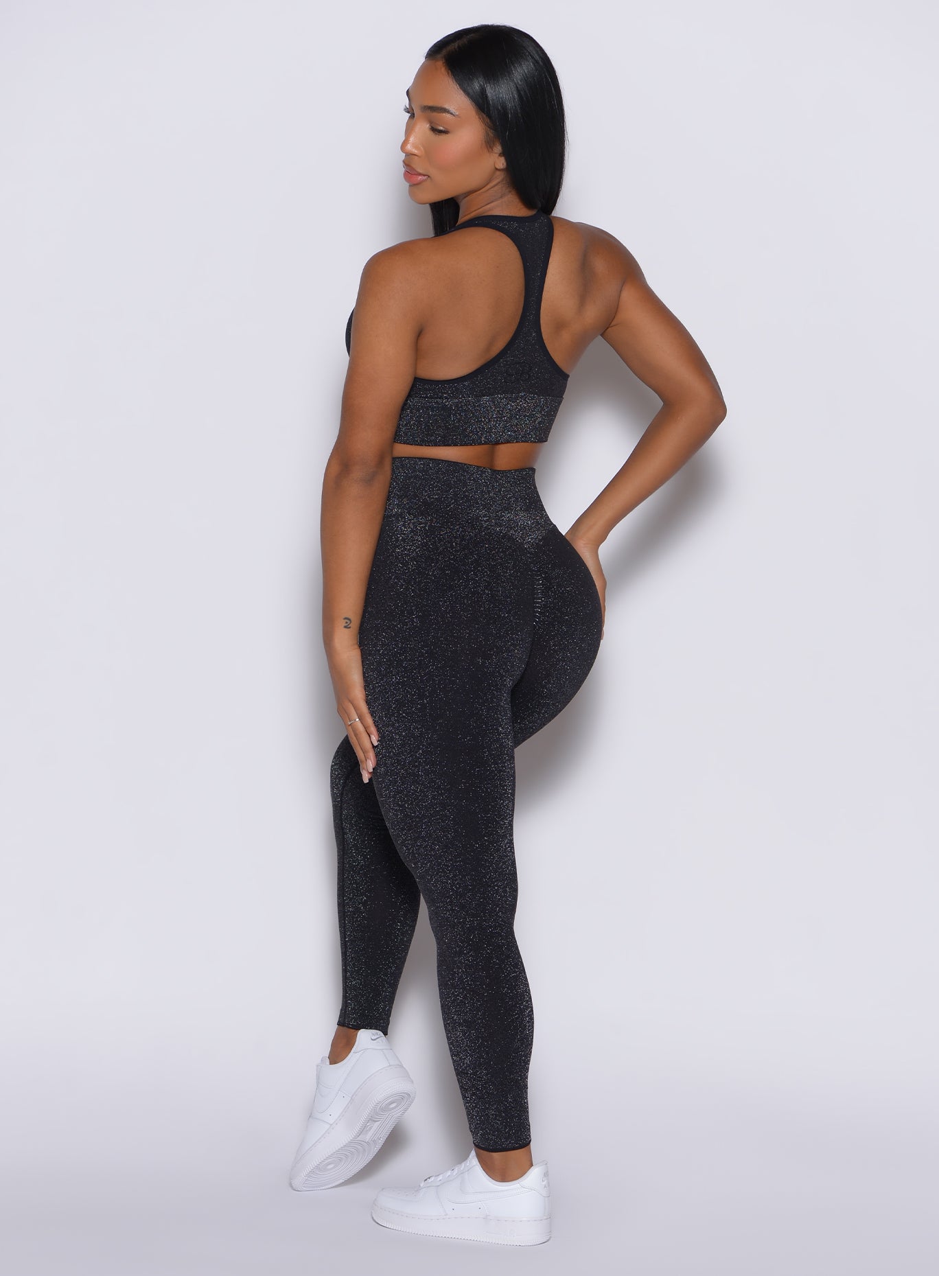 back side profile view of a model wearing our Shimmer Seamless Leggings in black sparkle color along with the matching shimmer bra
