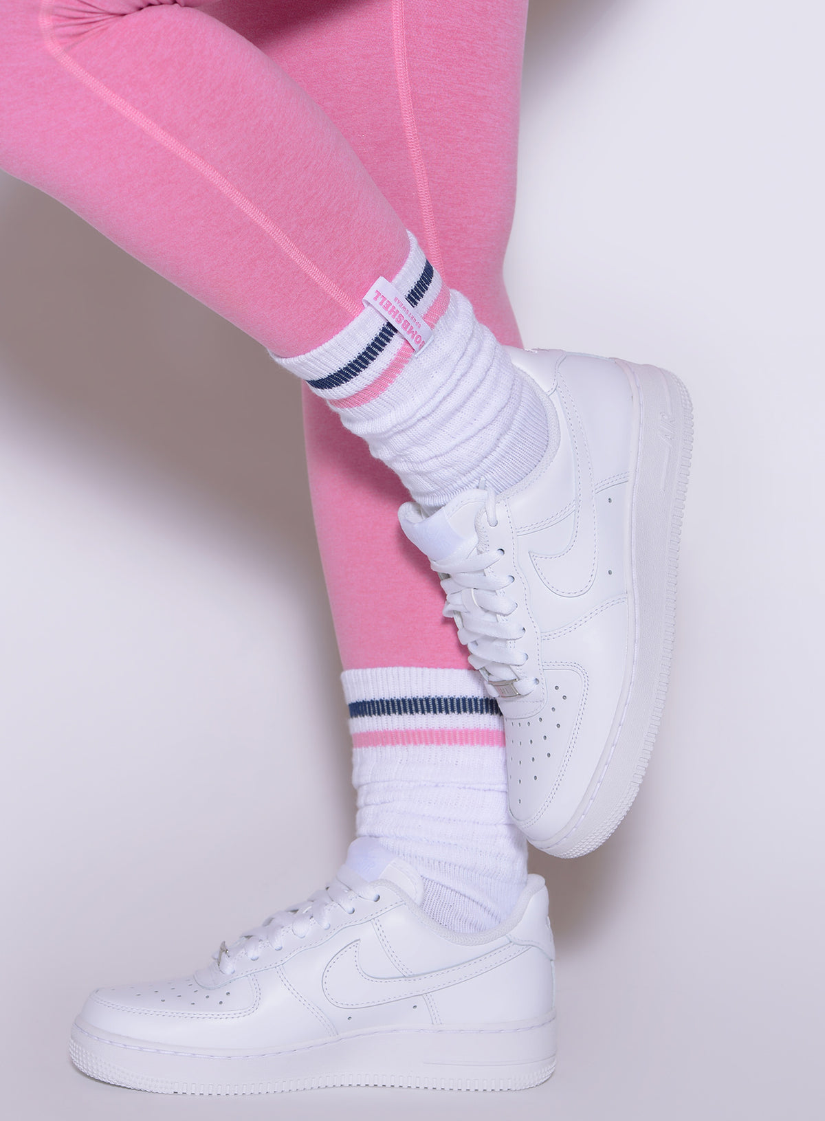 Bombshell Sportswear Pink Punch slouch socks with pink and navy stripes paired with sneakers.