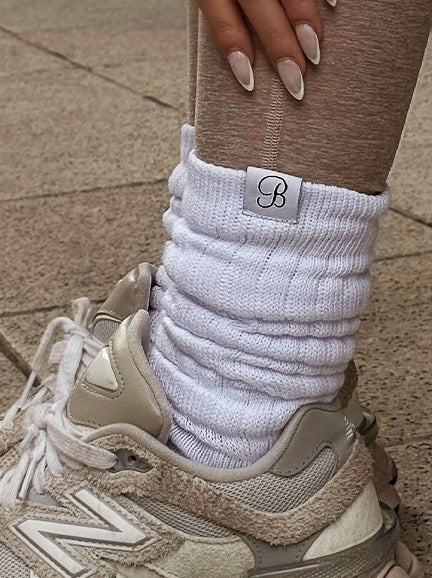 White sock with a brand logo worn with beige sneakers on a pavement background