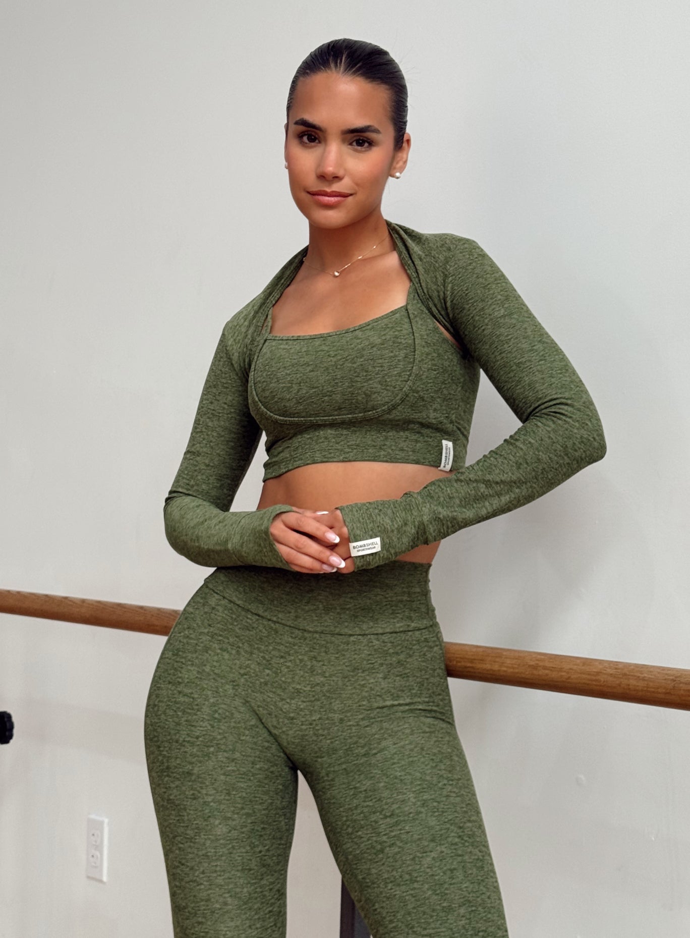A woman modeling a matching olive green activewear set consisting of a long-sleeve scoop-neck crop top and high-waisted leggings.