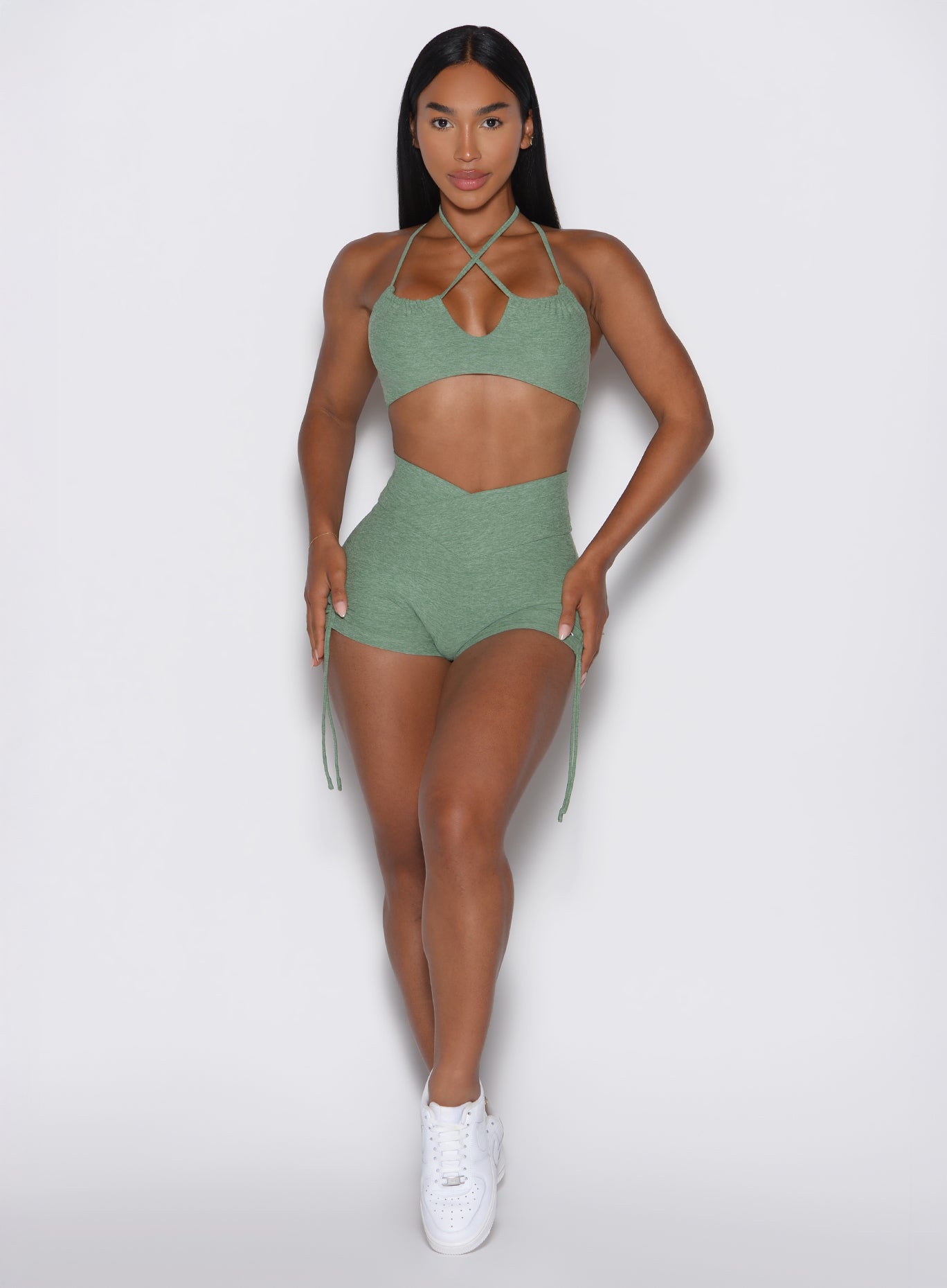 front profile view of a model with both hands resting on her thighs wearing the Tiny Waist Tie Shorts in basil color