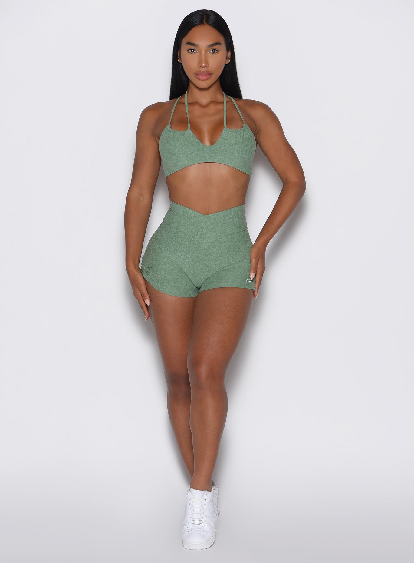 front profile view of a model with both hands resting on her thighs wearing the Tiny Waist Tie Shorts in basil color