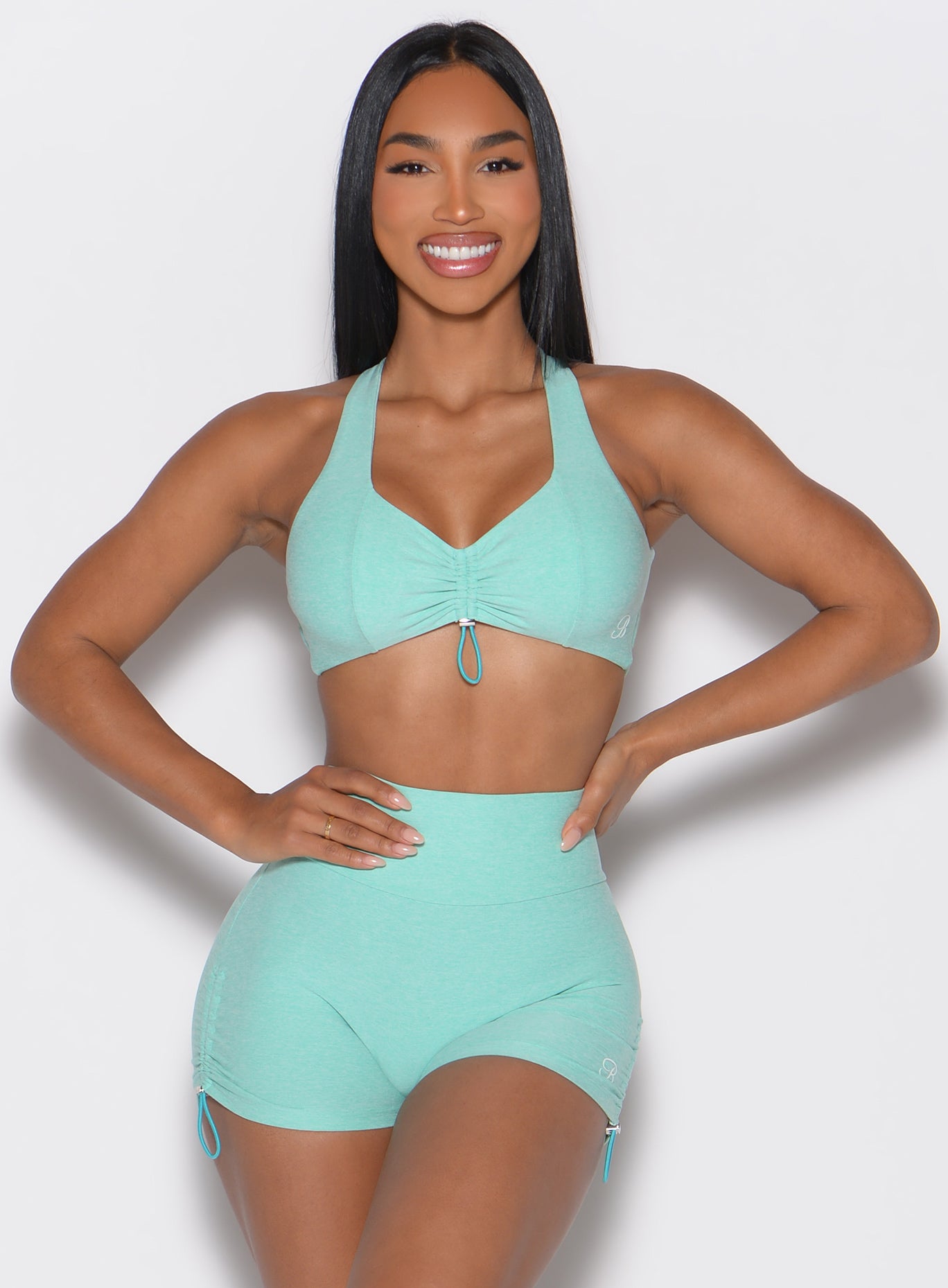 front profile view of a model with both hands on her waist wearing the Toggluxe bra in Oasis color
