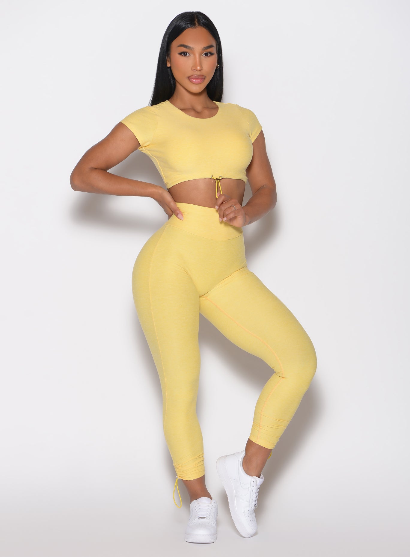 front right side profile view of a model holding the front toggle of the matching top wearing the Toggle Pull Leggings in Lemon color