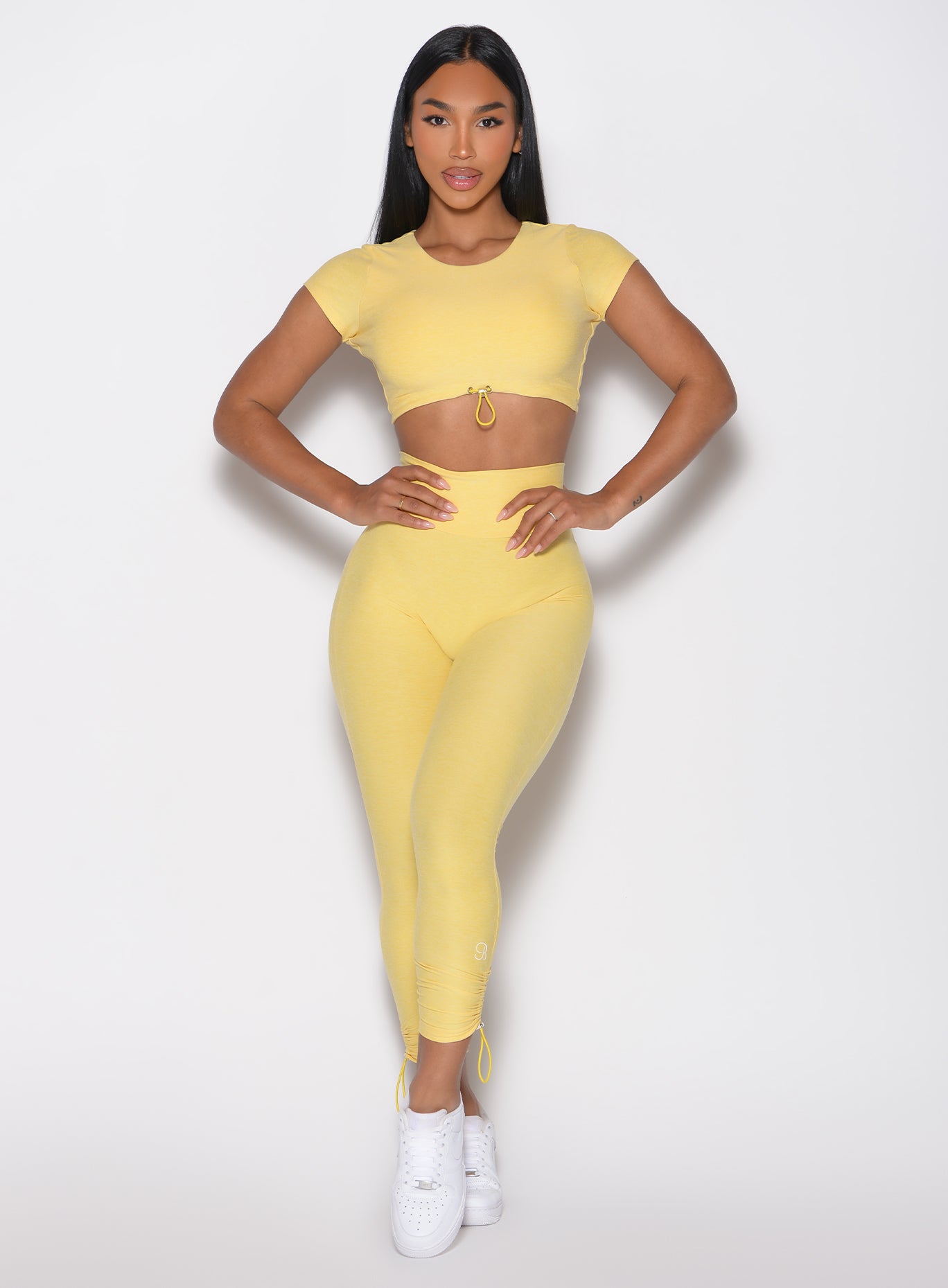 front profile view of a model with both hands on her waist wearing the Toggle Pull Leggings in Lemon color