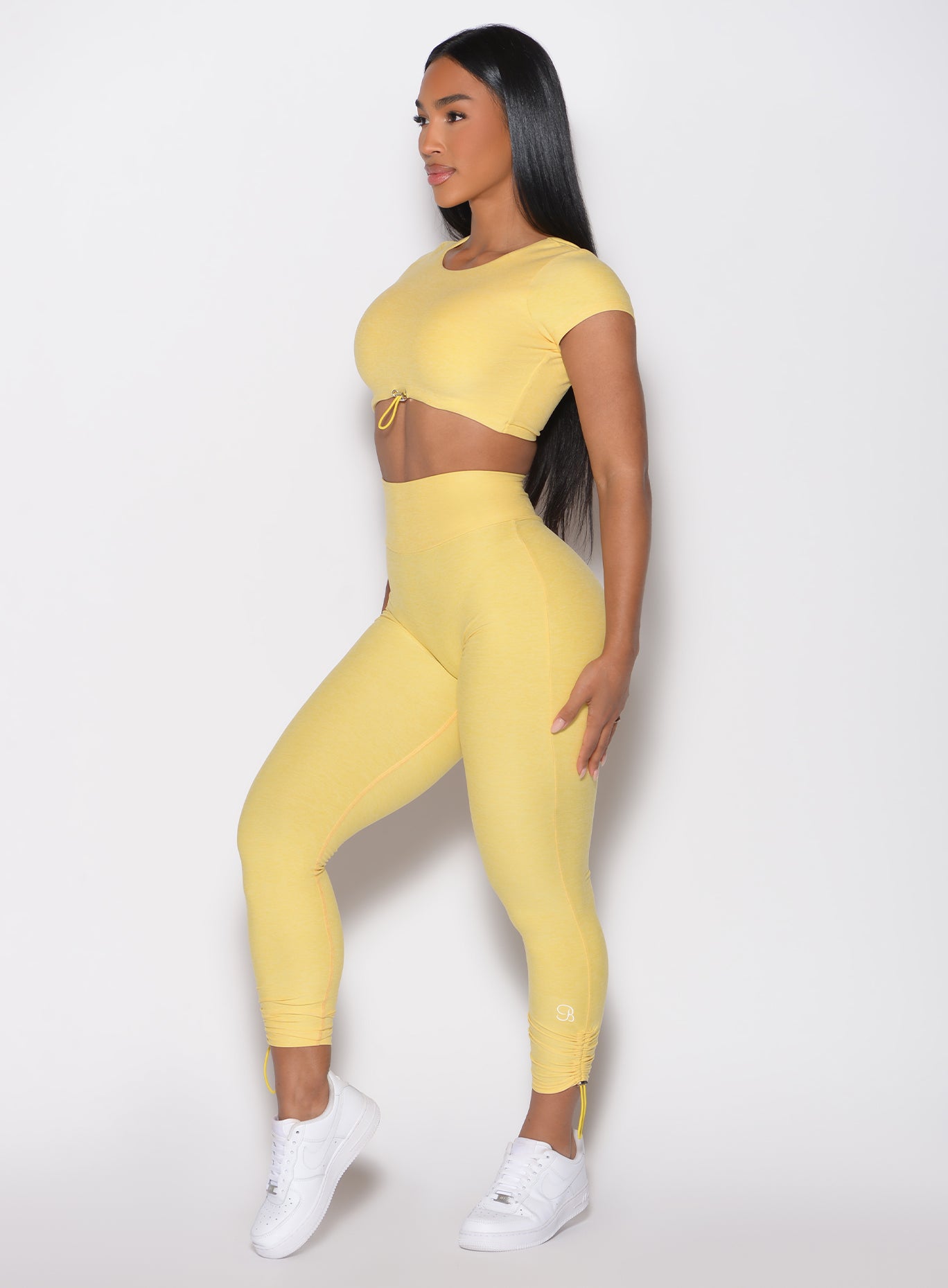 left side profile view of a model with both hands on her thighs wearing the Toggle Pull Leggings in Lemon color