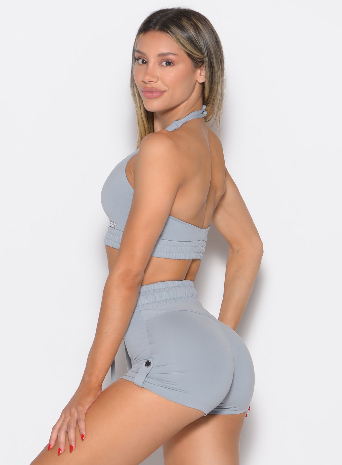 left side profile view of a model looking over her shoulder wearing the Trailblaze Sports bra in quarry color paired with the matching shorts