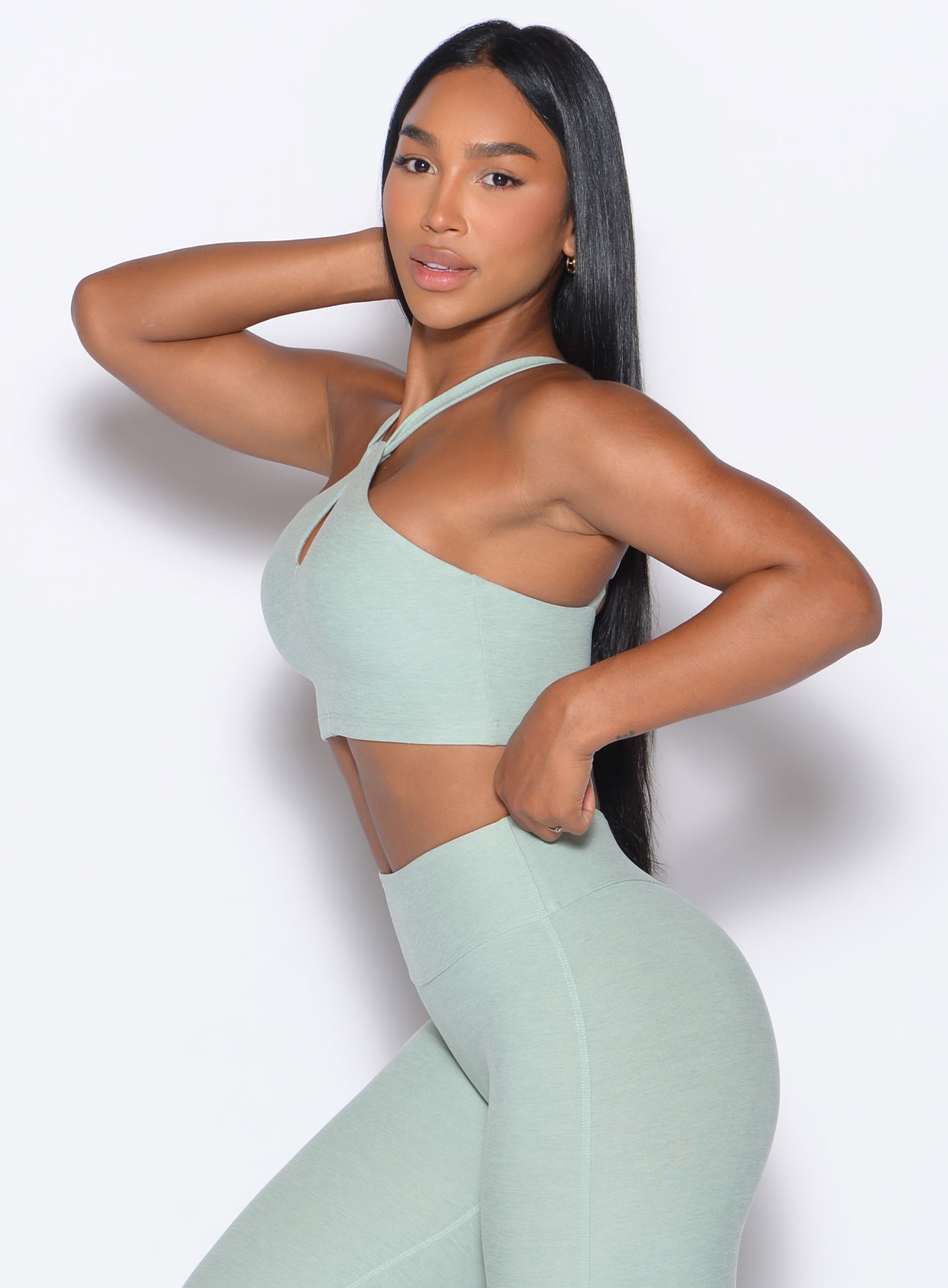 left side profile view of our model adjusting the waistband of the leggings wearing the Twist Up Bra in soft aloe color