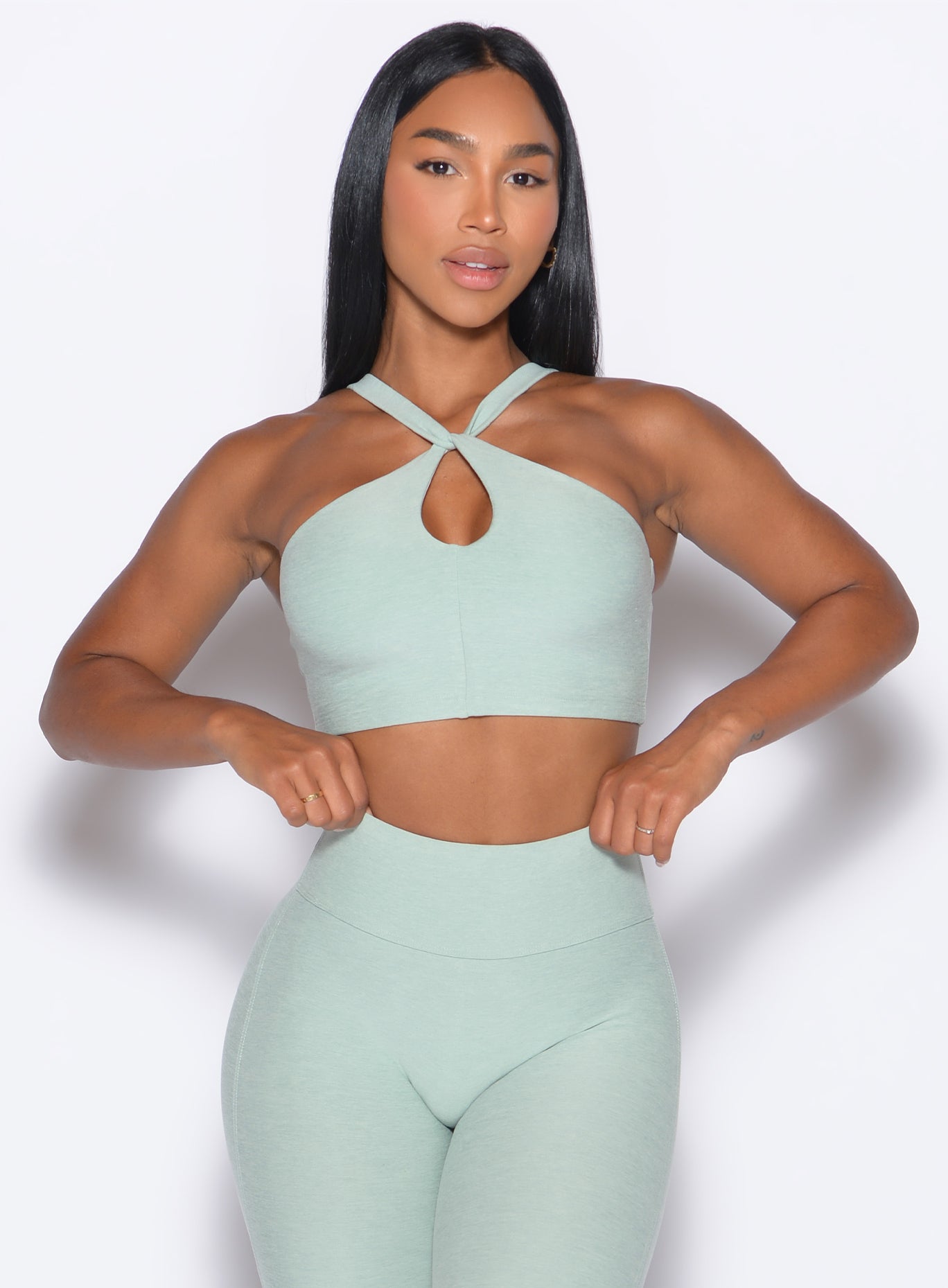 front profile view of our model adjusting the waistband of the leggings wearing our Twist Up Bra in soft aloe color