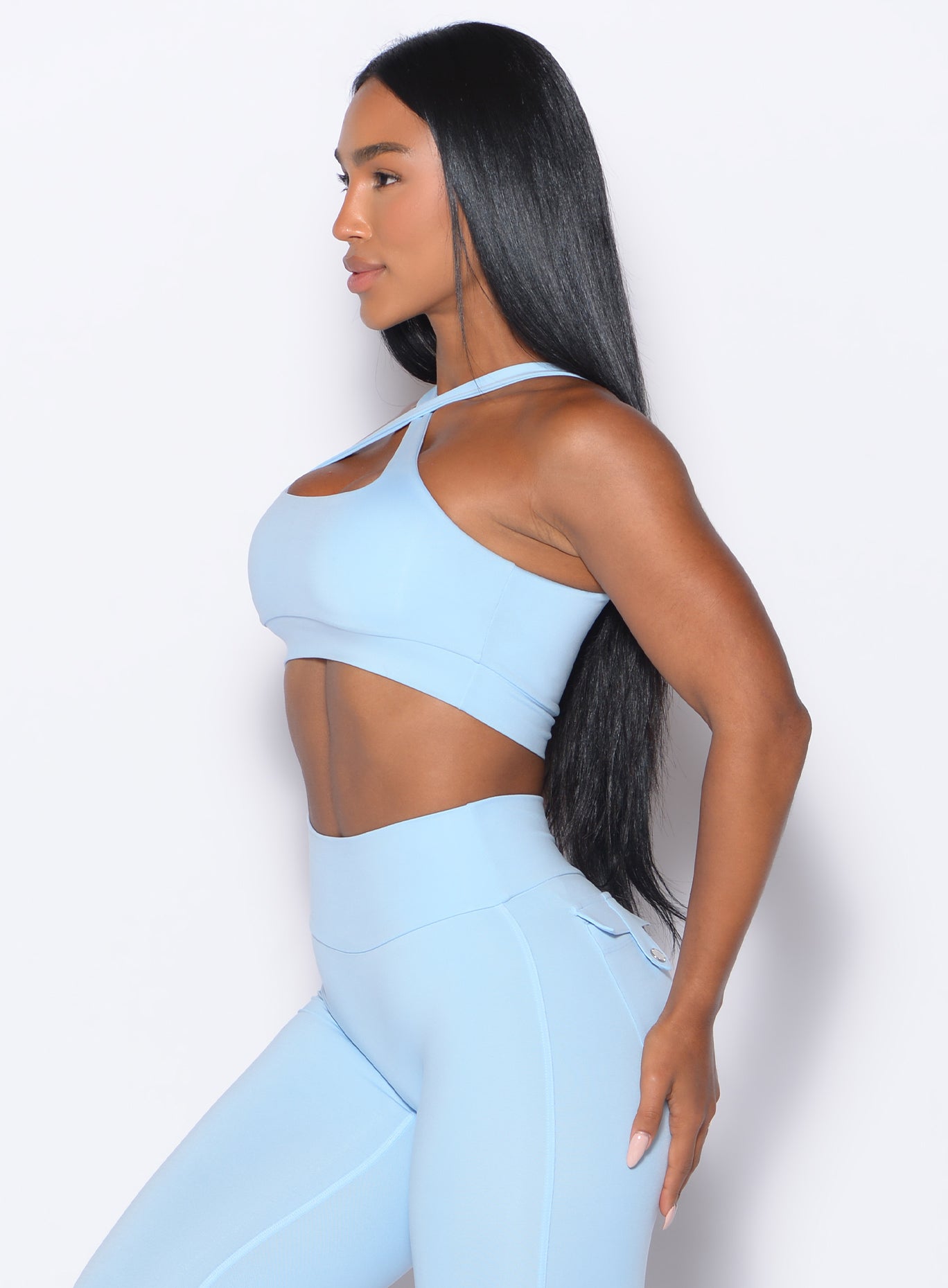 left side profile view of a model facing forward wearing our Two Way Bra in Glacial Blue color and a matching leggings