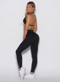 left side profile view of a model looking over her shoulder wearing our Uplift Peach Leggings in black color