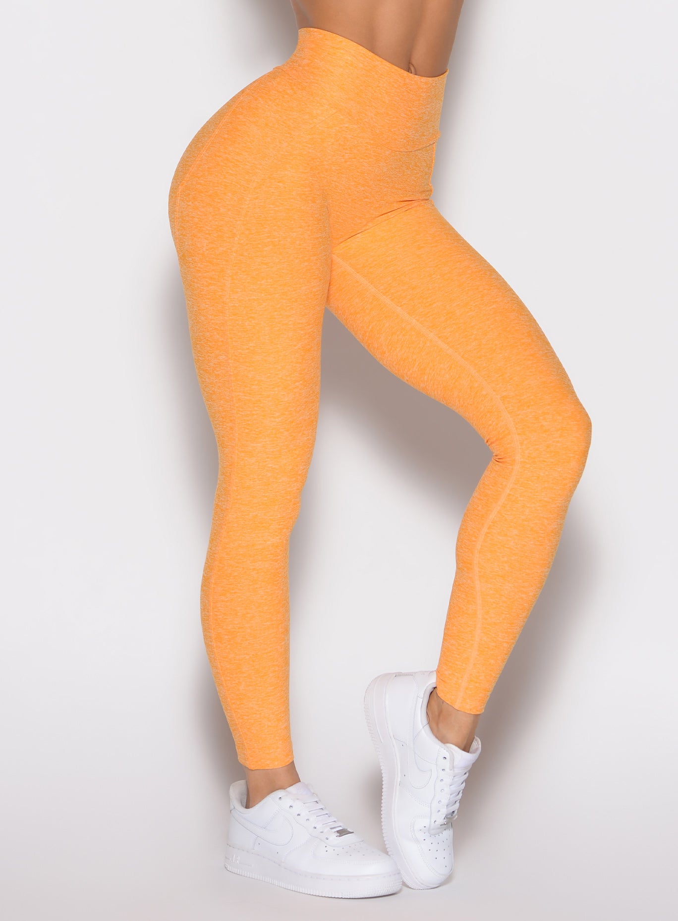 close up front right side profile view of a model wearing the Uplift peach leggings in kumquat color