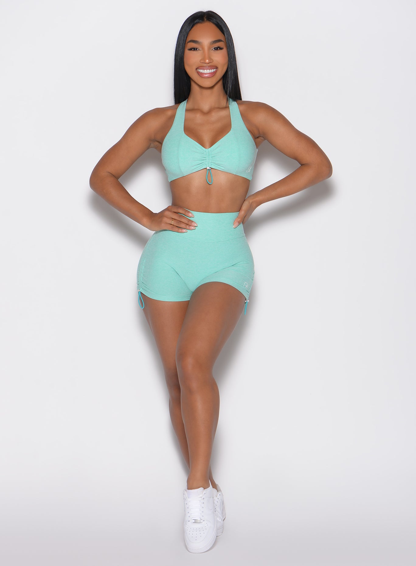 front profile view of a model with both hands on her waist wearing the V back toggle shorts in Oasis color
