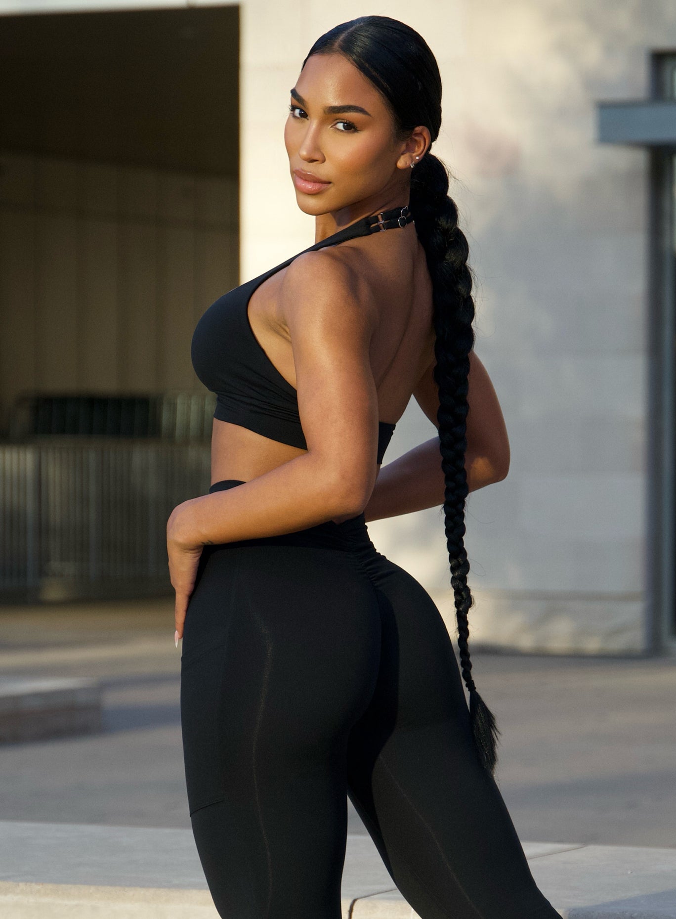Left side profile view of a model facing to her left wearing our black backless bra along with the v back leggings