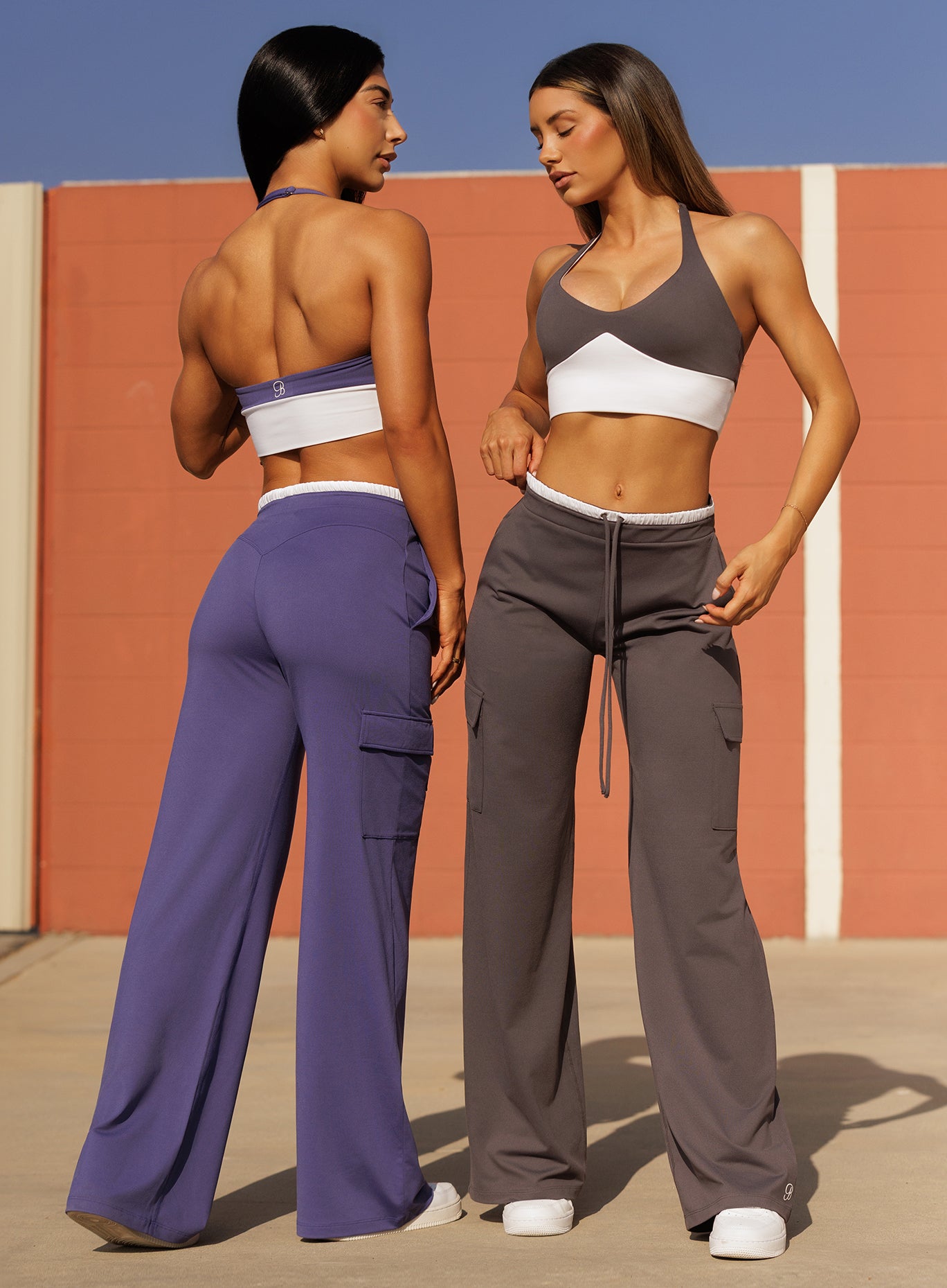 Front and back view of two models in outdoors wearing Bombshell Sportswear Confidence bra tops in Future Dusk and Champion Grey colors paired with matching wide leg joggers, featuring sculpting supportive fit and coordinated sets