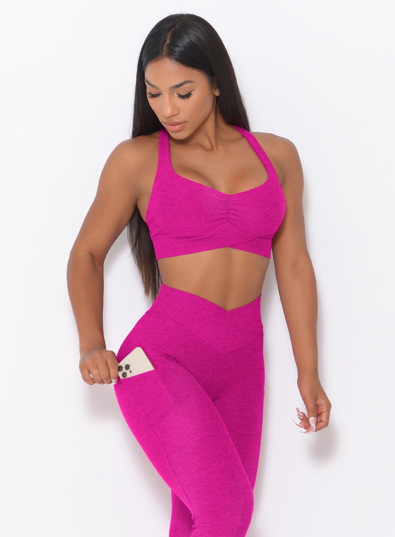front profile view of a model wearing our Angel Sports Bra in Ultra Pink color looking at the smartphone in her right pocket of the leggings