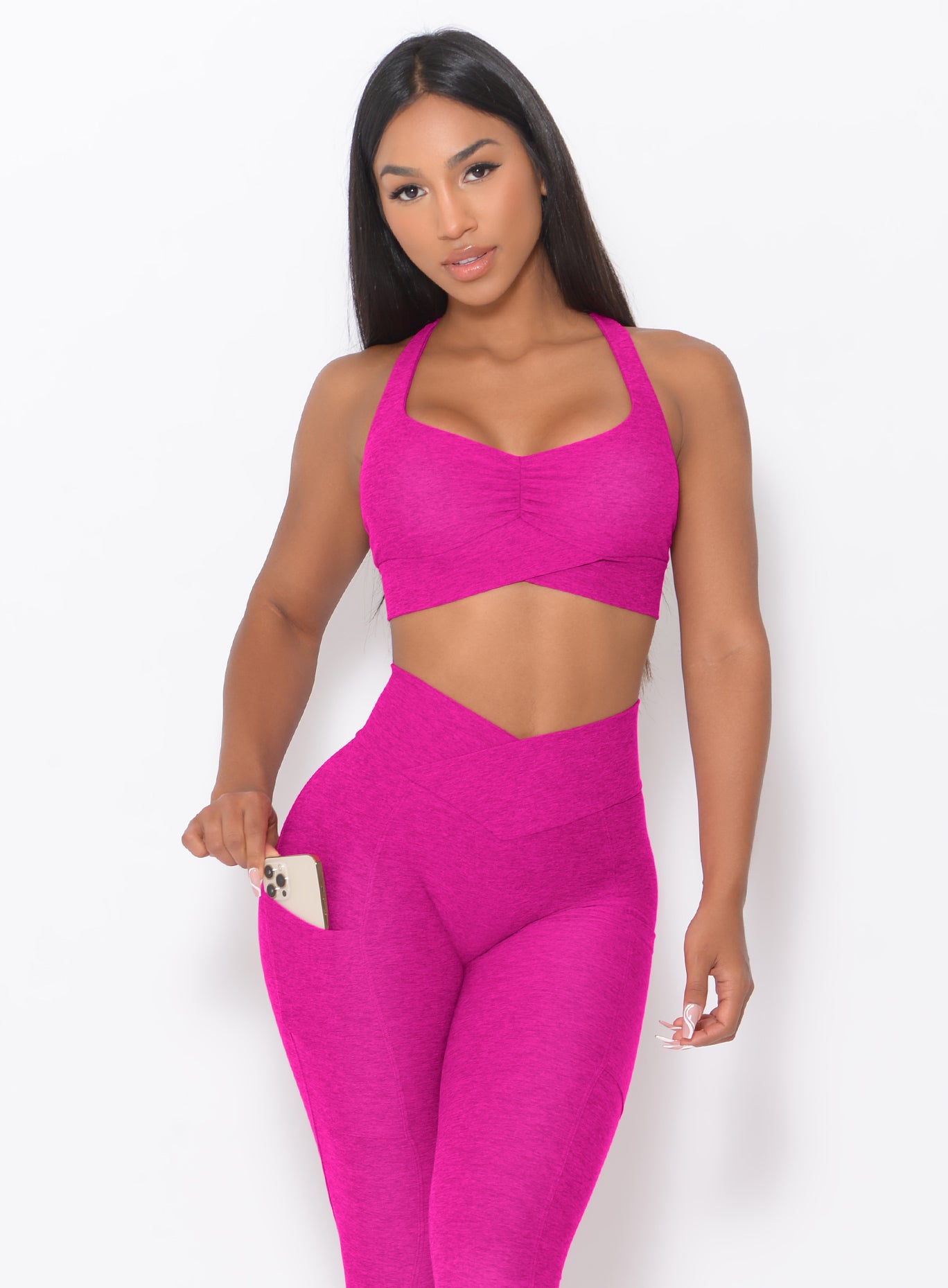 front profile view of a model wearing our Angel Sports Bra in Ultra Pink color holding the smartphone in her right pocket of the leggings