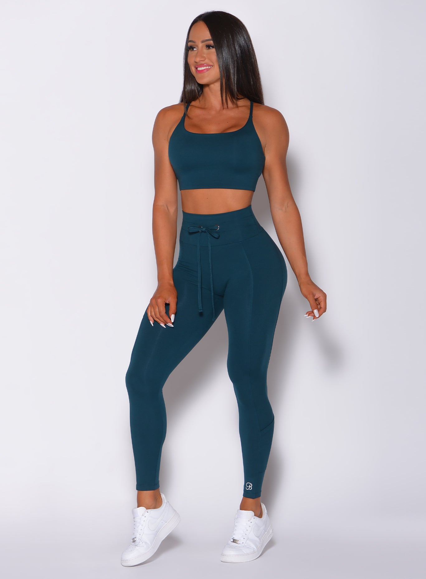 Front profile view of a model in our empower leggings in peacock color and a matching bra