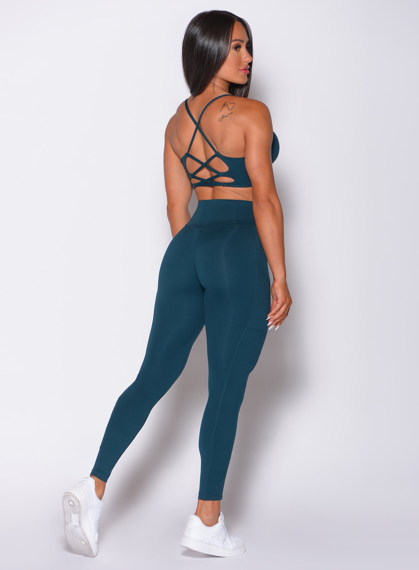 Back profile view of a model in our empower leggings in peacock color and a matching bra