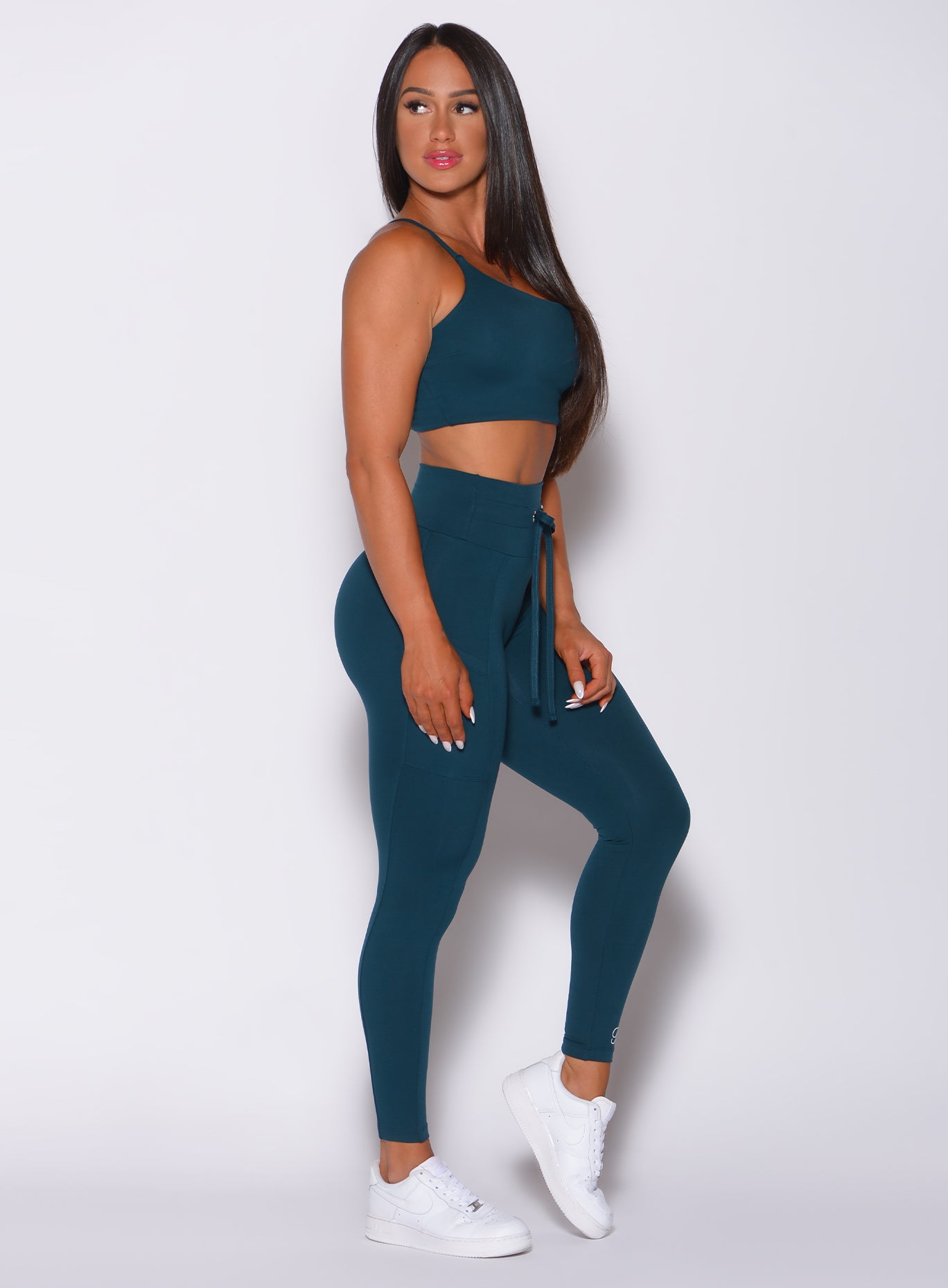 Right side profile view of a model facing to her right wearing our empower leggings in peacock color and a matching bra