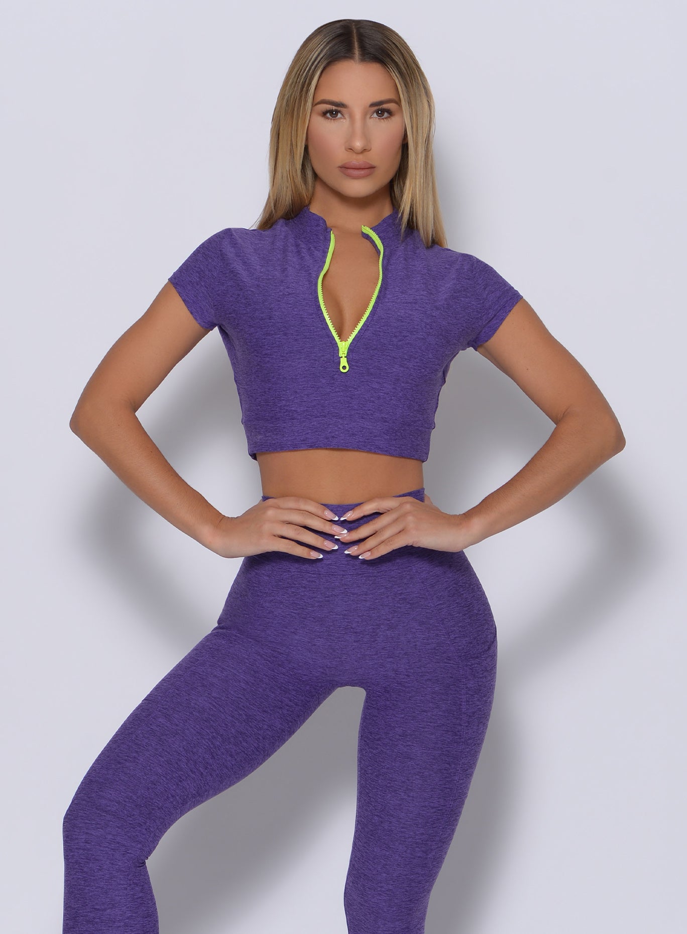 Front profile view of the model in our neon zip top in iris color and a matching leggings 