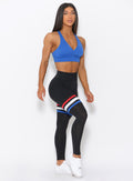 Right side view of the model angled right wearing our high waisted Scrunch Thigh high in black with three stripes on the thighs and a black sports bra