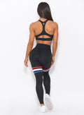Back view of the model wearing our Scrunch Thigh high in black with three stripes on the thighs and a black sports bra