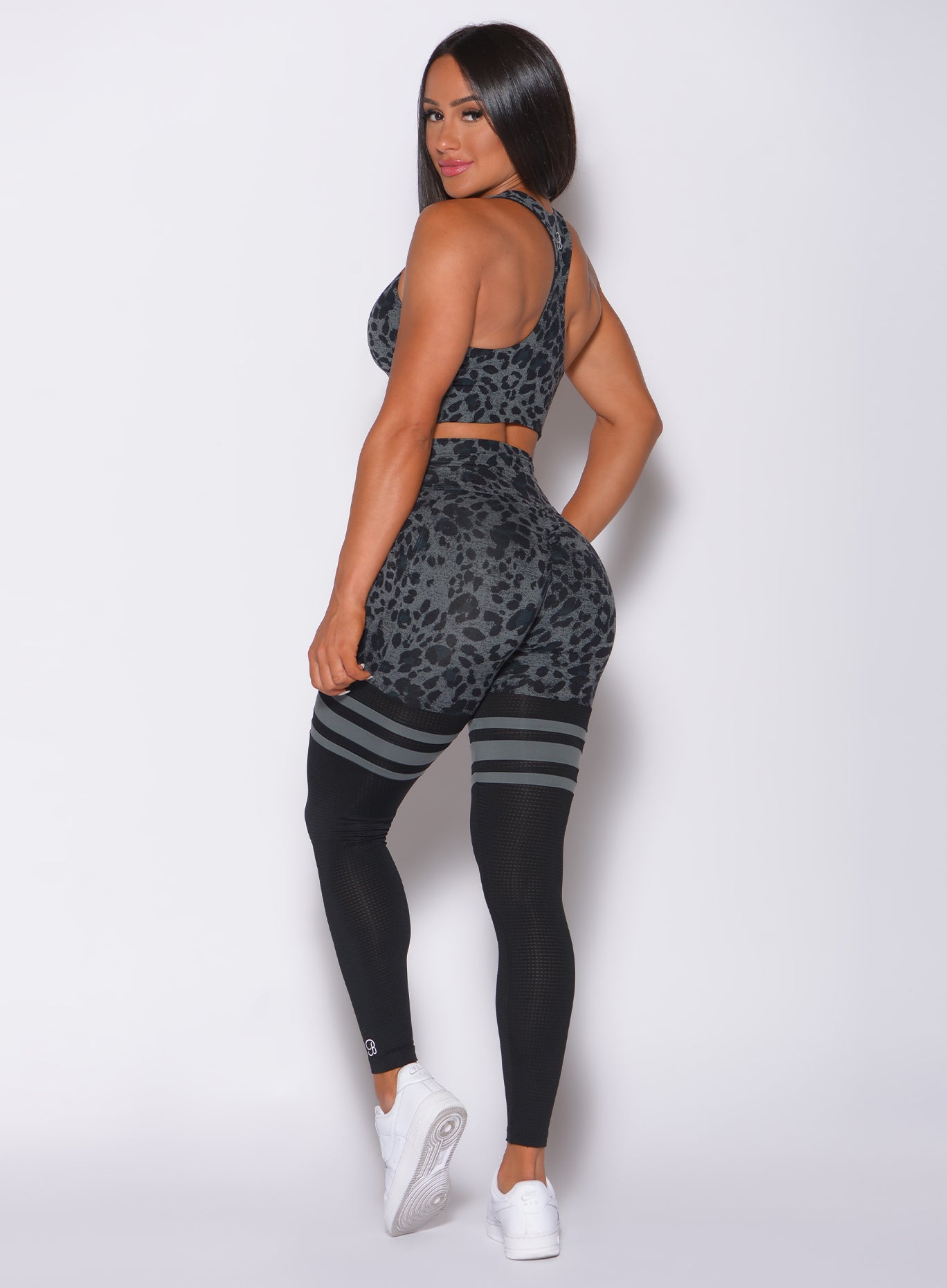 Left side profile view of a model in our scrunch thigh high in charcoal leopard print and a matching sports bra