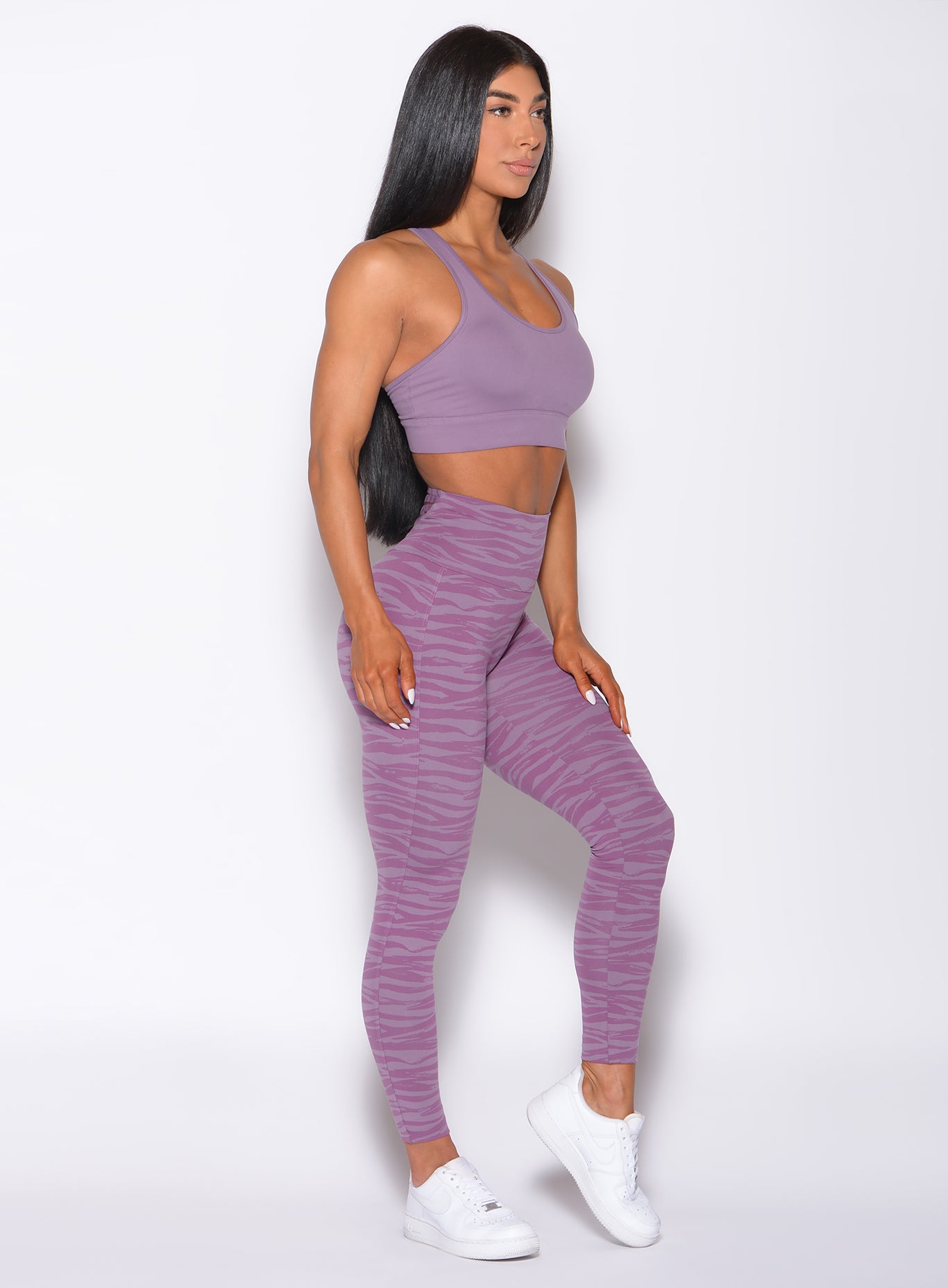 Right side  profile view of a model facing forward wearing our rival sports bra in solid orchid color and a matching sexy back leggings in tiger print