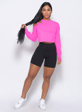 Front profile view of the model in our black pocket biker shorts and a neon pink pullover