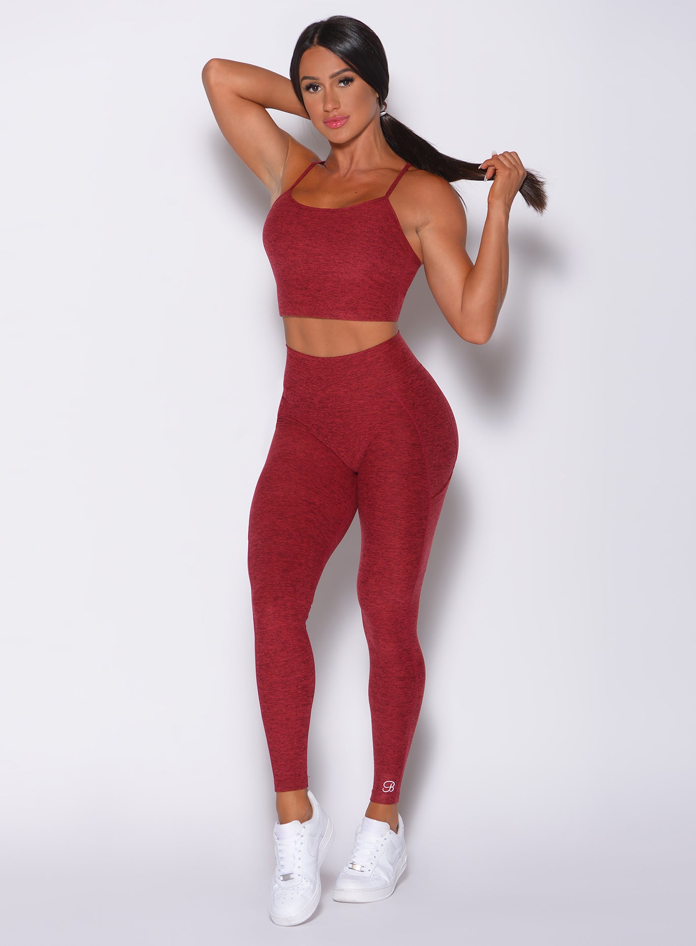 Front profile view of a model in our uplift pocket leggings in red rose color and a matching bra