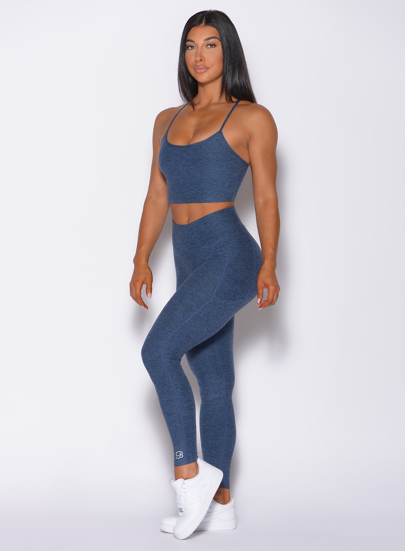 Left side profile view of a model angled left wearing our uplift pocket leggings in night sky color and a matching bra