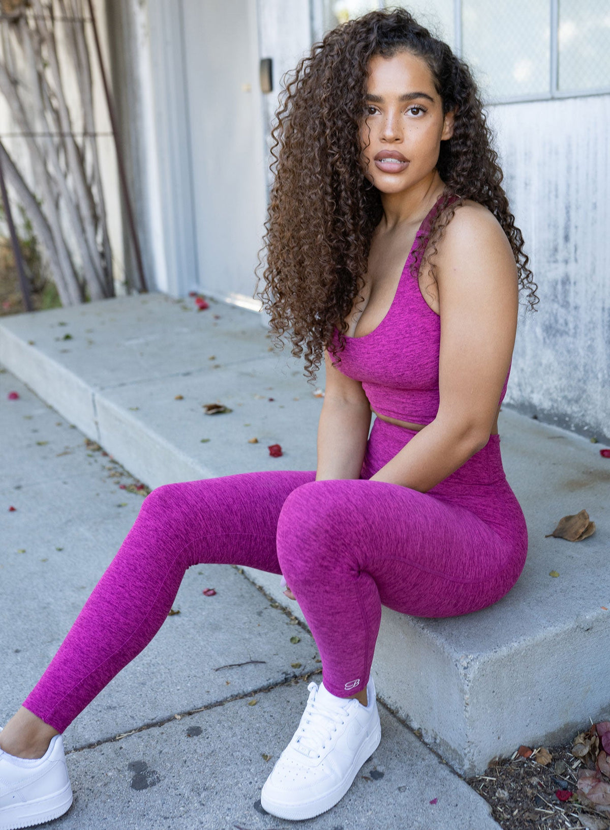 Model sitting on sidewalk in a bright pink activewear outfit