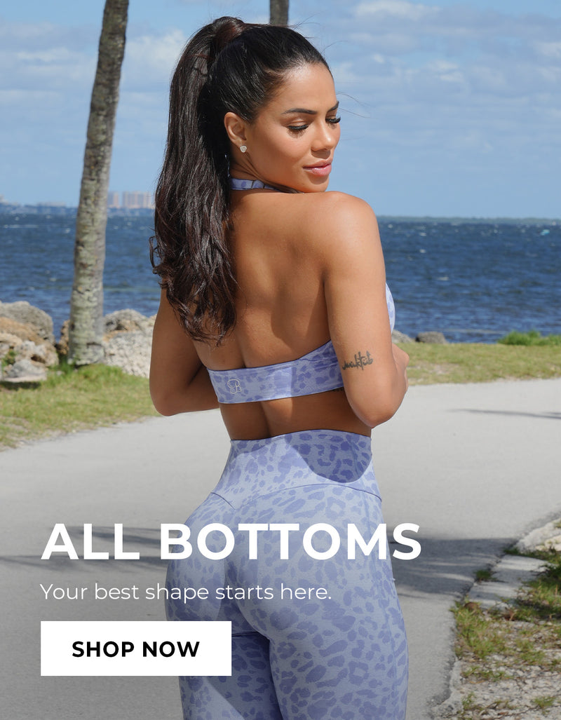 Woman in blue cheetah printed leggings and matching sports bra standing by a coastal path with text overlay. Text says ALL BOTTOMS tYour best shape starts here. SHOP NOW