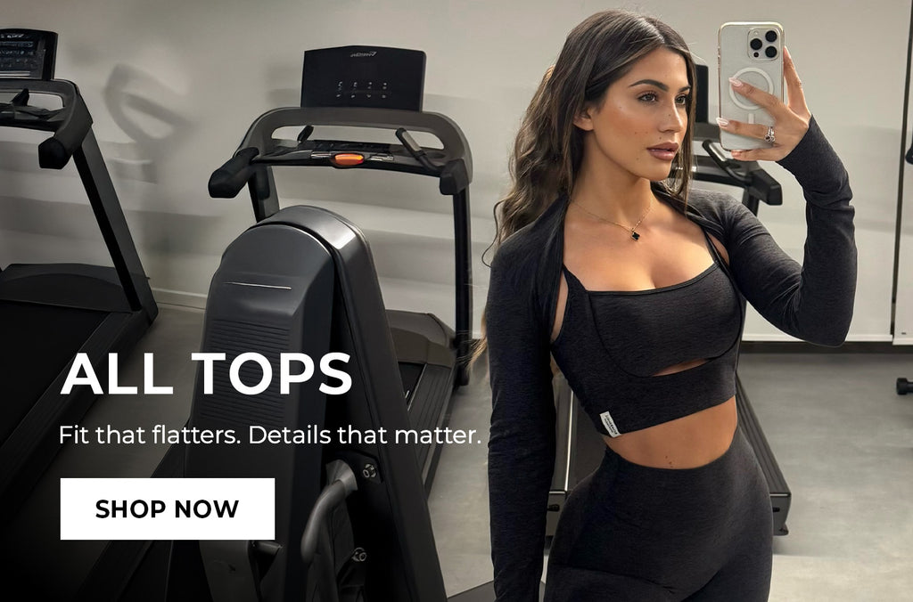 Woman in Heathered Black Bolero, Studio Sculpt Bra, and 7/8 leggings taking a mirror selfie in a gym setting with fitness equipment. Text overlay reads: 'ALL TOPS Fit that matters. Details matter.' CTA button: 'SHOP NOW'